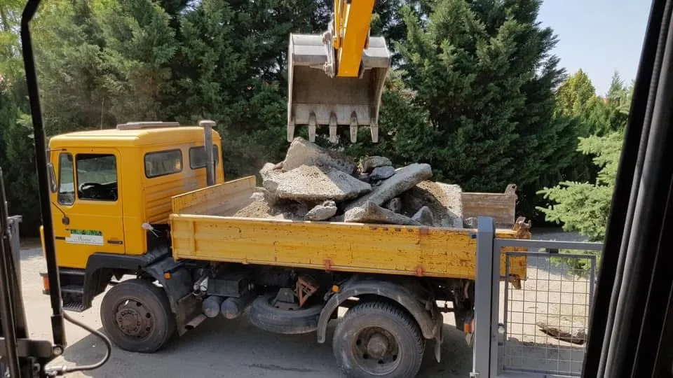 Sárga tehergépkocsi bontott törmelékkel, a kotró kanala fölötte